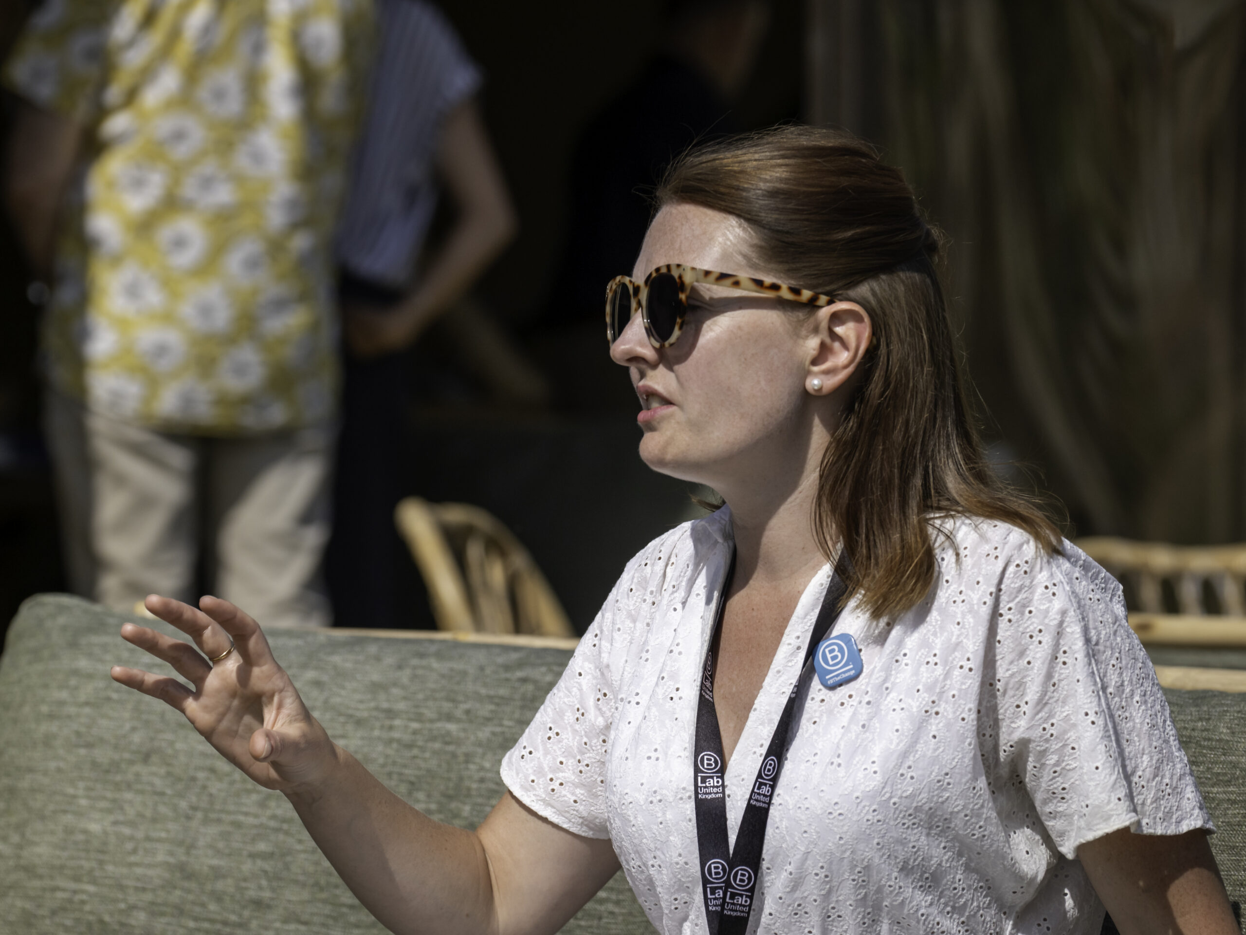 A b corp consultant in a white top, with sunglasses on a grey sofa outside